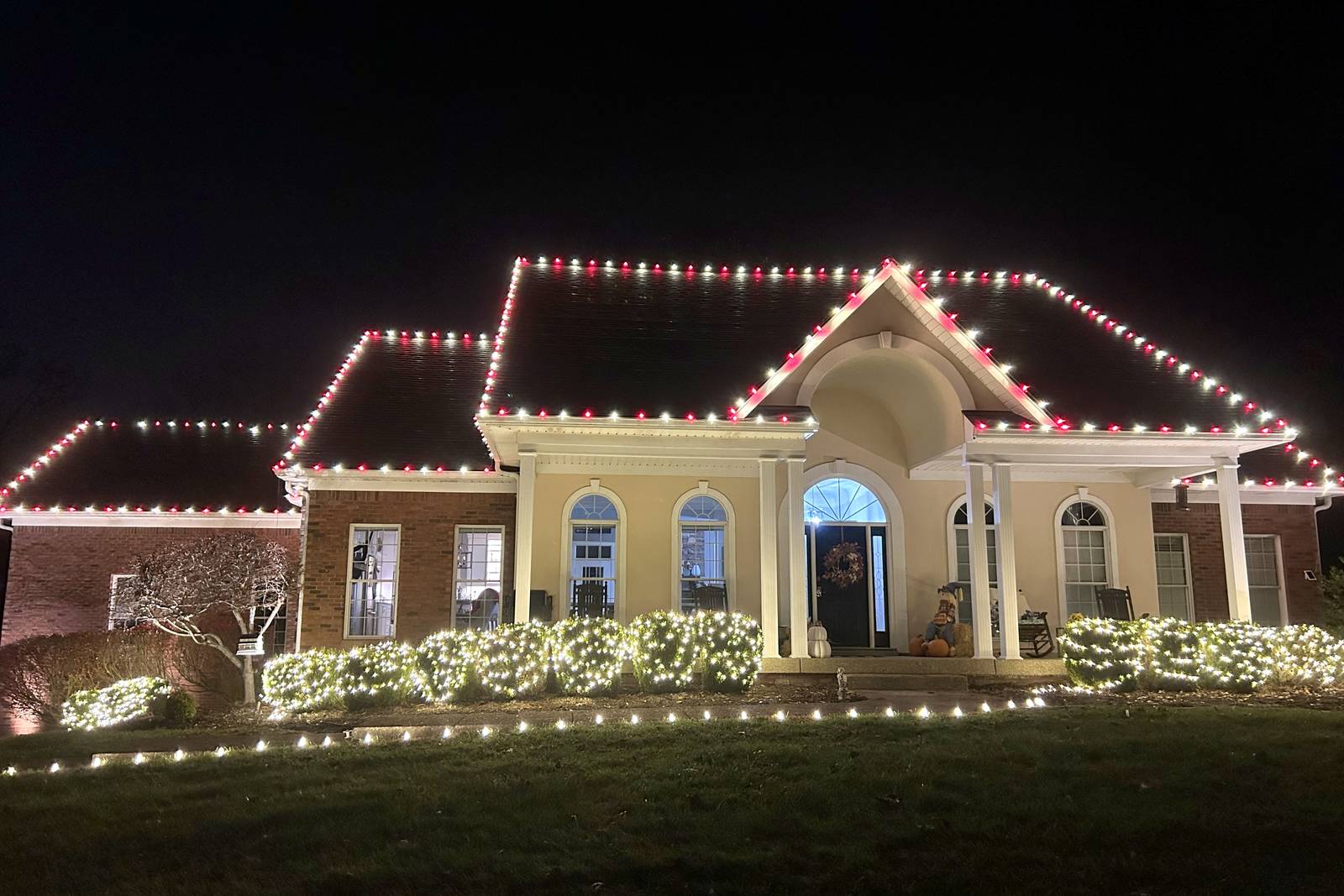Red and warm white alternating Christmas roofline lights with lit bushes and a lit wreath, Middletown, Kentucky