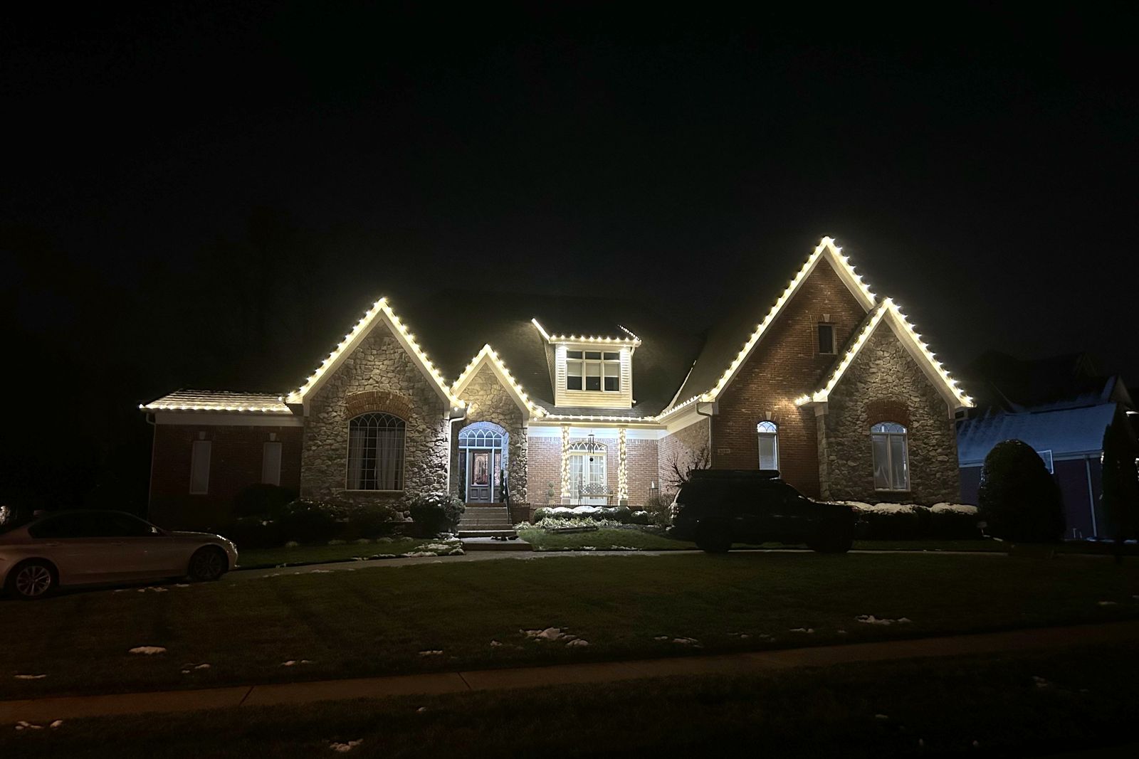 Warm white C9 Christmas lights along the roofline of a stone two-story home in Middletown, Kentucky
